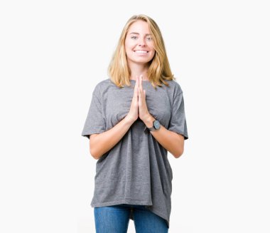 Ellerle birlikte AF emin gülümseyen için soran dua izole arka plan üzerinde büyük boy rahat t-shirt giyen güzel genç kadın.