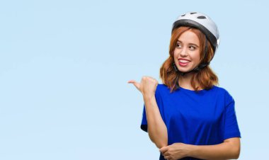 Seyir ve başparmak yanında yukarıyı mutlu yüz ile gülümseyen izole arka plan üzerinde bisikletçi kask giyen genç güzel kadın.