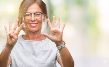 Orta yaş İspanyol kadın kıdemli gözlük gösterilen ve parmakları ile işaret izole arka plan üzerinde dokuz kendinden emin ve mutlu gülümseyerek iken numara.