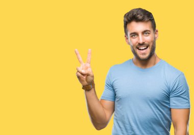 Mutlu yüz zafer işareti yaparken kameraya göz kırpıyor ile gülümseyen izole arka plan üzerinde genç yakışıklı adam. İki numaralı.