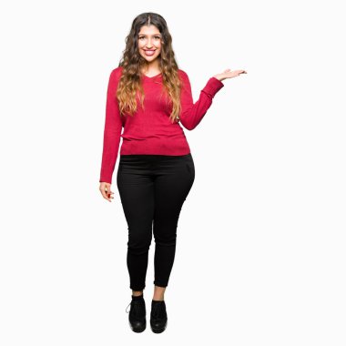 Neşeli sunulması ve kameraya bakarak avucunun ile işaret gülümseyen kırmızı kazak giyen genç güzel kadın.