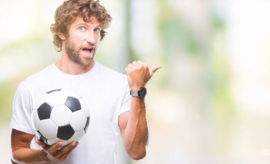 İşaret ve başparmak kadar mutlu yüz gülümseyen tarafı ile gösteren izole arka plan üzerinde futbol futbol topu tutan Latin asıllı yakışıklı modeli