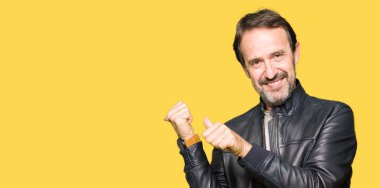 Siyah deri giyen orta yaş yakışıklı adam kendinden emin gülümseyen işaretleme için arkasından el ve başparmak yukarıya, ceket