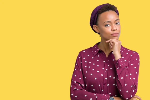 Beautiful young african american woman wearing head scarf over isolated background looking confident at the camera with smile with crossed arms and hand raised on chin. Thinking positive.