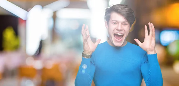 狂牛病と腕との成功のために狂気を祝う孤立の背景に青いセーターを着ている若いハンサムな男は 発生し 興奮して叫んで目を閉じた 勝者の概念 — ストック写真