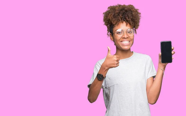 年轻的非洲裔美国妇女在孤立的背景显示智能手机屏幕高兴与灿烂的微笑做确定的标志 用手指竖起大拇指 优秀的标志 — 图库照片