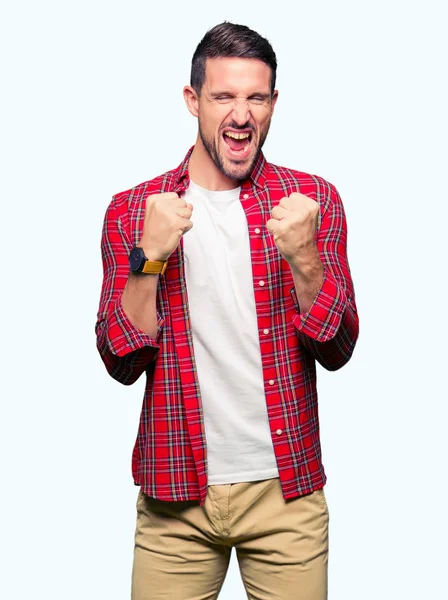 Gülümseyen ve başarı için çığlık çok mutlu ve heyecanlı kaldırdı, silah ile kazanan jest yapıyor rahat gömlek giymiş yakışıklı adam. Kutlama kavramı.