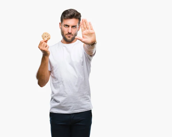 年轻英俊的男人吃巧克力片饼干在孤立的背景与开放的手做停止标志与严肃和自信的表情 防御手势 — 图库照片