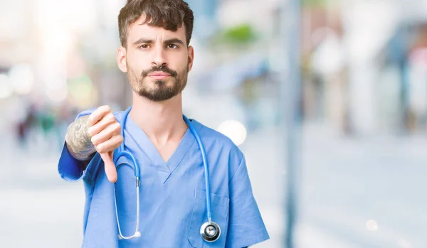 年轻英俊的护士男子穿着外科医生制服在孤立的背景看起来不高兴和愤怒 表现出拒绝和消极的大拇指向下的姿态 错误的表达 — 图库照片
