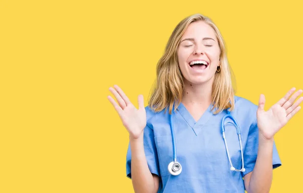 美丽的年轻医生妇女穿着医疗制服在孤立的背景庆祝疯狂和疯狂的成功与手臂抬起和闭上闭上的眼睛尖叫兴奋 优胜者概念 — 图库照片
