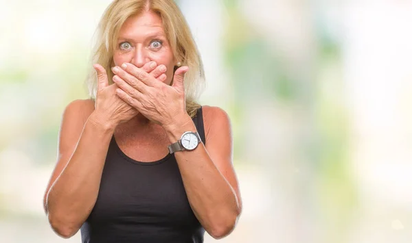 Middle age blonde woman over isolated background shocked covering mouth with hands for mistake. Secret concept.