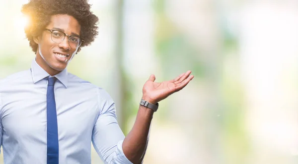 Afro american business man wearing glasses over isolated background smiling cheerful presenting and pointing with palm of hand looking at the camera.