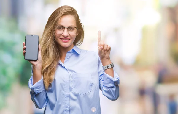 Young beautiful blonde business woman showing screen of smartphone over isolated background surprised with an idea or question pointing finger with happy face, number one