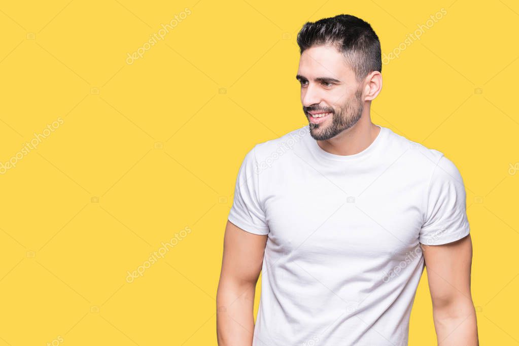 Young man wearing casual white t-shirt over isolated background looking away to side with smile on face, natural expression. Laughing confident.