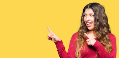 Genç güzel kadın kırmızı kazak giyen gülümseyen ve iki elleri ve parmakları ile tarafına işaret kamera bakıyor.