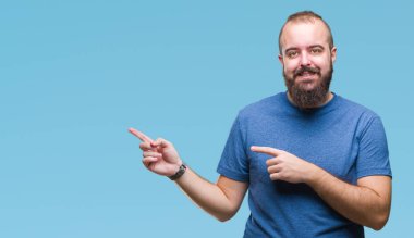 Kameraya bakarak yan el ve parmak ile işaret eden genç beyaz hipster adam yüzünde kocaman bir gülümseme ile izole arka plan üzerinde.