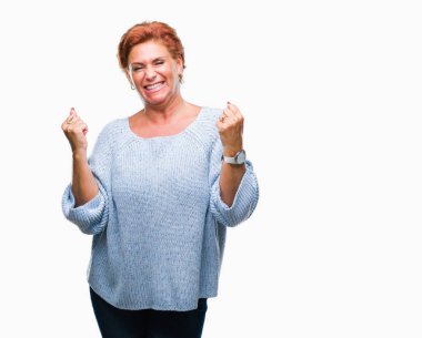 Üzerinde kış kazak giyen Atrractive üst düzey beyaz Kızıl saçlı kadın şaşırmış ve başarı için hayran kaldırdı kollarını açarak kutlama arka plan izole ve gözleri açık. Kazanan kavramı.