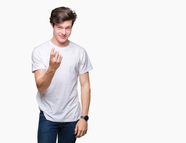 Beckoning gel burada mutlu ve gülümseyerek el davet ile jest izole arka plan üzerinde rahat beyaz t-shirt giyen genç yakışıklı adam