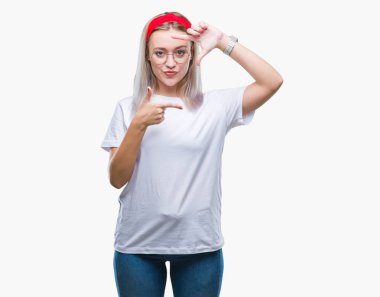 Elle yapma çerçeve ve parmakları ile mutlu yüz gülümseyen izole arka plan üzerinde gözlüklü sarışın genç kadın. Yaratıcılık ve Fotoğrafçılık kavramı.