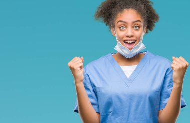 İzole arka plan kutlama üzerinde genç afro Amerikalı doktor kadın şaşırttı ve başarı için kaldırdı kollarını açarak hayret ve gözleri açık. Kazanan kavramı.