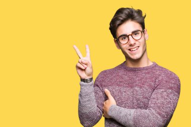 Mutlu yüz zafer işareti yaparken kameraya göz kırpıyor ile gülümseyen izole arka plan üzerinde gözlük takan yakışıklı delikanlı. İki numaralı.