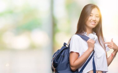 Sürpriz yüz işaret parmağı kendini izole arka plan üzerinde sırt çantası ve kulaklıklar giyen genç Asyalı kadın