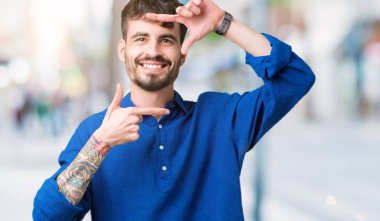 Yakışıklı delikanlı elle yapma çerçeve ve parmakları ile mutlu yüz gülümseyen izole arka plan üzerinde. Yaratıcılık ve Fotoğrafçılık kavramı.