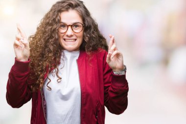 Güzel esmer kıvırcık saçlı Genç kız umut ve gözleri kapalı geçiş parmaklarıyla gülümseyen izole arka plan üzerinde ceket ve gözlük takıyor. Şans ve batıl kavramı.