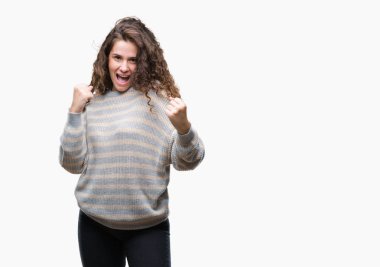 Gülümseyen ve başarı için çığlık izole arka plan çok mutlu ve heyecanlı kaldırdı, silah ile kazanan jest yapıyor üzerinde kış kazak giyen güzel esmer kıvırcık saçlı Genç kız. Kutlama kavramı.