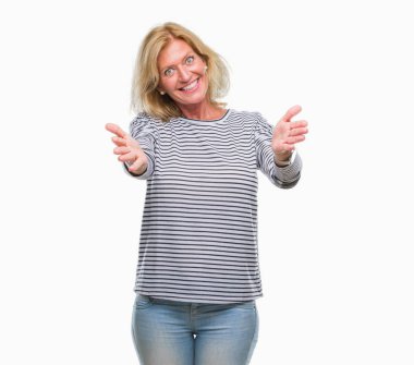 Orta yaş sarışın kadın sarılmak için kollarını açarak gülümseyerek kameraya bakarak izole arka plan yüzünden. Neşeli ifade kucaklayan mutluluk.