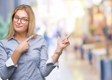 Gülümseyen ve iki elleri ve parmakları ile tarafına işaret kamera bakarak izole arka plan üzerinde gözlük takan Genç beyaz iş kadını.