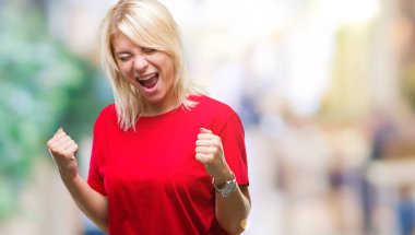 Gülümseyen ve başarı için çığlık çok mutlu ve heyecanlı kaldırdı, silah ile kazanan jest yapıyor izole arka plan üzerinde kırmızı t-shirt giyen genç güzel sarışın kadın. Kutlama kavramı.