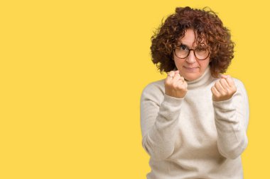 Güzel orta ager kadın kıdemli giyen boğazlı kazak ve izole arka plan üzerinde gözlük yumruk savunma hareketi, kızgın ve üzgün yüz, sorunu korkuyor ile savaşmaya hazır