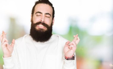 Uzun saç ve sakal geçiş parmakları umut ve gözler gülümseyen sportif sweatshirt giyen genç adamla kapalı. Şans ve batıl kavramı.