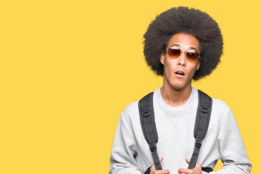 Güneş gözlüğü ve sırt çantası bir sürpriz yüz, korkuyor ve heyecanlı korku ifadesi ile şok korkmuş afro saçlı genç Afro-Amerikan adam