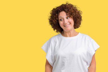 Görünümlü yan ve dik dik bakma uzağa düşünce gülümseyen izole arka plan üzerinde beyaz t-shirt giyen güzel orta ager üst düzey kadın.