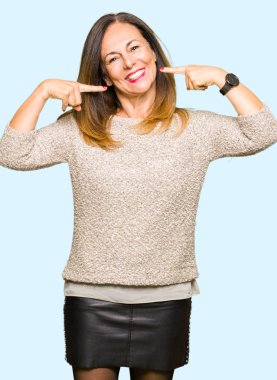 Kendinden emin gösterilen ve işaret parmakları diş ve ağız ile gülümseyen moda kazak giyen güzel orta yaş kadın. Sağlık kavramı.