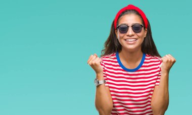 Genç güzel Arap kadın izole arka plan kutlama üzerinde güneş gözlüğü takıyor şaşırttı ve başarı için kaldırdı kollarını açarak hayret ve gözleri açık. Kazanan kavramı.