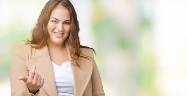 Artı boyutu genç kadın giyiyor kış ceket izole arka plan üzerinde güzel Beckoning gel burada mutlu ve gülümseyerek el davet ile jest