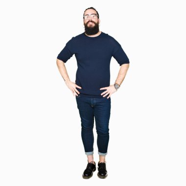 Uzun saç ve sakal uzak tarafına yüzünde, doğal ifade gülümseme ile seyir gözlüklü genç hipster adam. Kendine güvenen gülüyor.