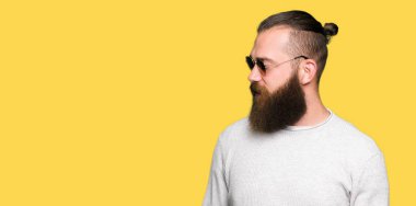 Genç hipster adam uzak tarafına yüzünde, doğal ifade gülümseme ile seyir güneş gözlüğü takıyor. Kendine güvenen gülüyor.