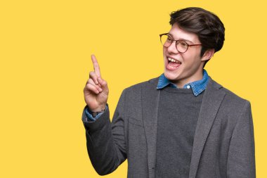 Yüzünde kocaman bir gülümseme ile izole arka plan üzerinde gözlük takan genç yakışıklı iş adamı kameraya bakarak yan el ve parmak ile işaret.