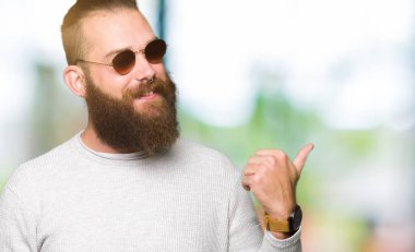 Genç hipster adam arıyor ve başparmak yanında yukarıyı mutlu yüz ile gülümseyen güneş gözlüğü takıyor.
