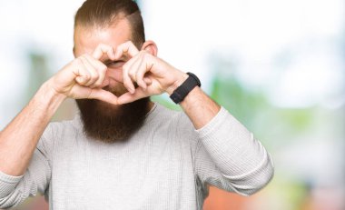 Casual kazak yapıyorsun kalp şekli el ve parmak işareti seyir gülümseyen ile giyen genç sarışın adam