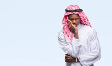 Geleneksel keffiyeh seyir yorgun ve bıkkın ile depresyon sorun Çapraz kollar ile izole arka plan düşünme üzerinde giyen genç Arapça Afrika adam.