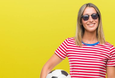 Futbol futbol topu ayakta ve diş gösterilen kendine güvenen bir gülümsemeyle gülümseyerek mutlu bir yüz ile izole arka plan üzerinde tutan genç güzel kadın