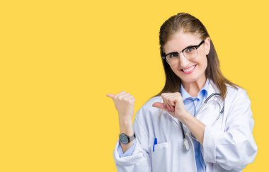 Orta yaş olgun doktor kadın üzerinde tıbbi bir palto giyiyor izole arka plan emin gülümseyen arkasından el ve kadar başparmak ile işaret