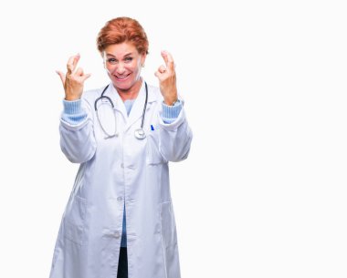 Umut ve gözleri kapalı geçiş parmaklarıyla gülümseyen izole arka plan üzerinde tıbbi üniforma giyen üst düzey beyaz doktor kadın. Şans ve batıl kavramı.