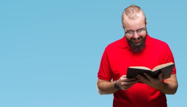 Gözlük takan ve ayakta ve diş gösterilen kendine güvenen bir gülümsemeyle gülümseyerek mutlu bir yüz ile izole arka plan üzerinde bir kitap okuma genç hipster adam