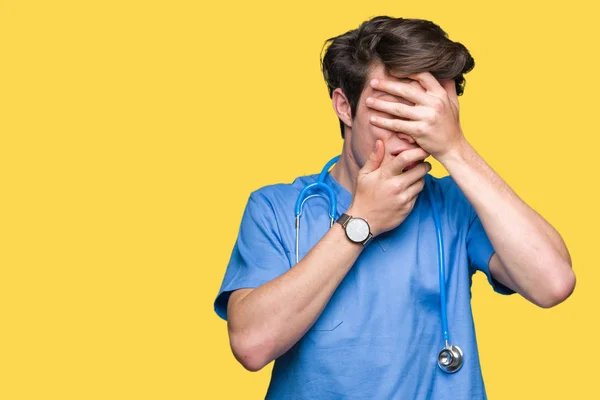 年轻的医生穿着医疗制服在孤立的背景覆盖眼睛和嘴巴与手 惊讶和震惊 隐藏情感 — 图库照片